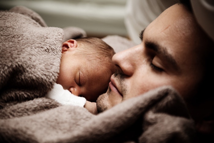 A stay at home dad laying with newborn baby