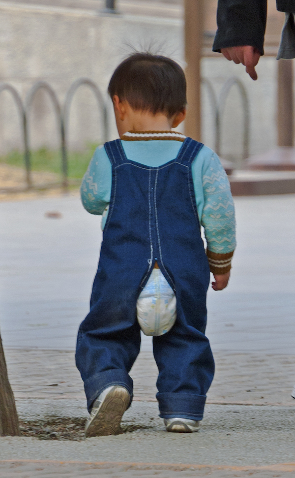 A toddler boy with pull up poking out of pants