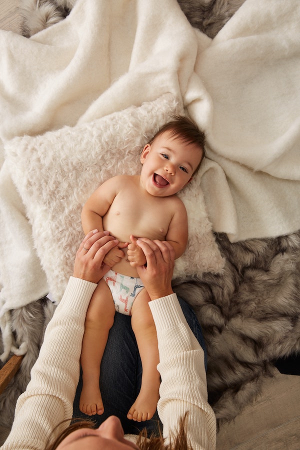 Baby laying on bed with mom tickling