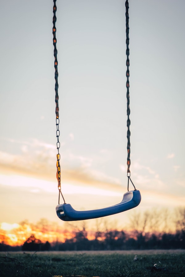 A rusty swing with chain hanging against the sunset